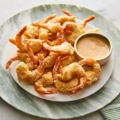 A plate piled high with golden-brown shrimp tempura, served with a small bowl of creamy dipping sauce.