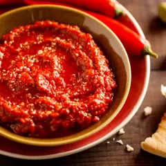 Pikantny sos adżika w miseczce, obok papryczek chili i oliwek. Idealny do pieczywa.