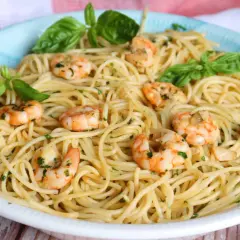 Un plato de espaguetis con gambas, adornado con hojas de albahaca fresca y perejil picado.
