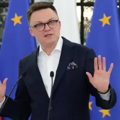 Szymon Hołownia w garniturze przemawia przed flagami Polski i UE.