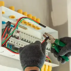 Elektryk w rękawicach pracuje przy skrzynce z bezpiecznikami. Zastanawiasz się, ile zarabia pomocnik elektryka na godzinę?