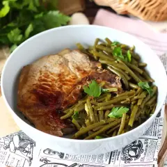 Une savoureuse côte de porc grillée accompagnée de haricots verts frais et persil, servie dans un bol blanc.