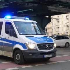 Polizeivan mit Blaulicht fährt auf der Straße. Ein polizeiliches Verkehrszeichen ist auf dem Fahrzeug angebracht.