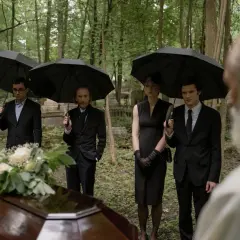 Smutne pożegnanie na pogrzebie w imieniu zmarłego. Rodzina i przyjaciele, pod czarnymi parasolami, żegnają bliską osobę przy trumnie.