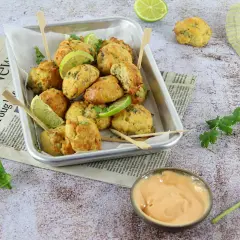 Plateau de délicieux accras dorés, garnis de quartiers de citron vert et de coriandre fraîche, servis avec une sauce crémeuse.