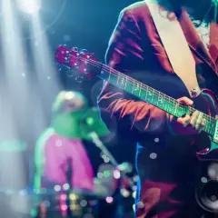 Koncertowy gitarzysta grający na scenie, przypominający klimatem piosenki lat 90. W tle perkusista.