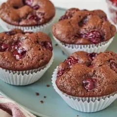 Schoko Kirsch Muffins auf einem blauen Teller, mit Kirschen garniert. Ein Genuss für jeden Schokoladenliebhaber.