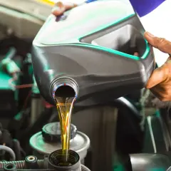 Main tenant verse le moteur de la voiture pour faire vidange voiture. L'huile neuve coule d'une bouteille dans le réservoir.