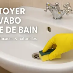 Main blanche avec robinet chromé, une main gantée de jaune utilise une éponge pour nettoyer le lavabo de la salle de bain. Astuces efficaces pour nettoyer le lavabo.
