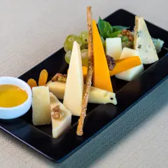 Piatto nero con assaggio di formaggi: caciotta, blu, cheddar, accompagnati da uva, noci, albicocche secche e miele.