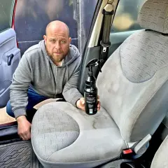 Mężczyzna z butelką środka do czyszczenia przygotowuje się do prania podsufitki w samochodzie.