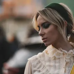 Blonde Frau mit auffälligem Make-up und einem grünen Haarband, das ihre Frisur betont.
