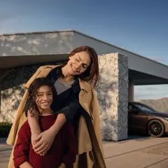 Madre e hija sonríen frente a una casa moderna con un Mercedes. El mantenimiento de tu Mercedes es clave para estos momentos.