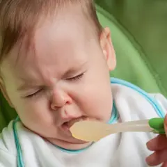 Dziecko z grymasem na twarzy, któremu podawany jest pokarm na łyżeczce.