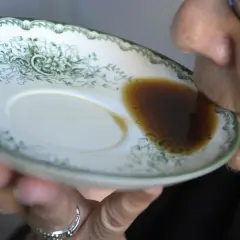 En person dricker gammalt kaffe direkt ur en tefat med grön dekor.