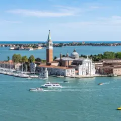 Widok na wyspę San Giorgio Maggiore w Wenecji, z kościołem i dzwonnicą. Wokół pływają łodzie, w tym prom.