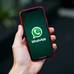 Dłoń trzyma iPhone'a z logo WhatsApp. Dowiedz się, jak przenieść czaty WhatsApp z Androida na iPhone.
