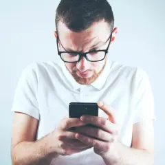 Zastanawiasz się, skąd firma windykacyjna ma Twój numer telefonu? Mężczyzna w okularach patrzy zdezorientowany na ekran smartfona.