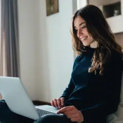Jeune femme souriante travaillant sur son ordinateur portable, rédigeant sa lettre de motivation master MEEF.