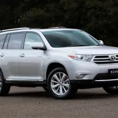 Srebrny Toyota Kluger zaparkowany na drodze, z ciemnym tłem drzew.