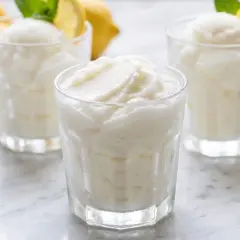 Tres vasos de sorbete de limón refrescante, con limones amarillos y hojas de menta al fondo.