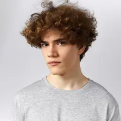 Joven con un peinado rizos hombre, cabello castaño y rizado, viste camiseta gris.