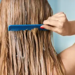 Une main peigne des cheveux blonds humides, recouverts d'un masque argile avant coloration végétale.