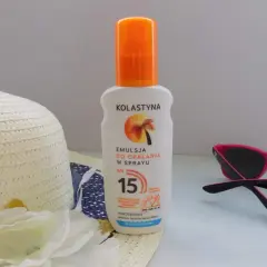 Emulsja do opalania w sprayu Kolastyna SPF 15 z karotenoidami, wodoodporna. Obok kapelusz i okulary przeciwsłoneczne.