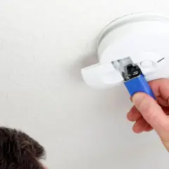 Ein Mann wechselt die Batterie des Rauchmelders, da diese leer ist.
