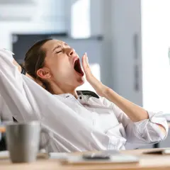 Erschöpfte Frau gähnt am Schreibtisch. Müdigkeit und Antriebslosigkeit können Anzeichen für einen L-Carnitin Mangel sein.
