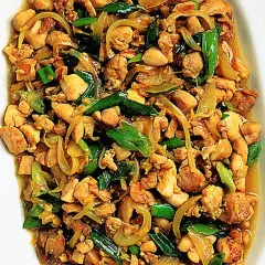 En närbild av en skål med saftig kyckling citrongräs, wokad med lök och gröna lökar.