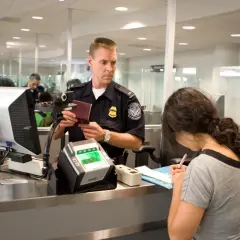 Funkcjonariusz sprawdza paszport kobiety przy stanowisku check-in na lotnisku.