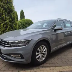 Szary Volkswagen Passat Variant z polskimi tablicami rejestracyjnymi stoi na podjeździe z kostki brukowej, otoczony zielenią.