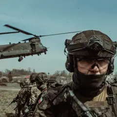 Żołnierze w pełnym rynsztunku, gotowi do akcji podczas szkolenia wojskowego. W tle widać helikopter transportowy.