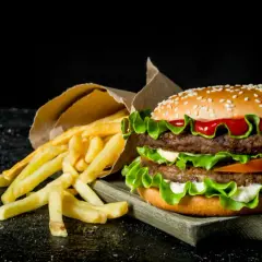 Podwójny hamburger z frytkami na ciemnym tle.