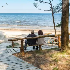 Para odpoczywa na ławce przy plaży, ciesząc się widokiem morza. Idealne miejsce na relaks w sanatorium nad morzem.