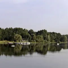 Spokojne jezioro Przeczyckie z odbijającymi się w wodzie drzewami i żaglówkami przy brzegu.