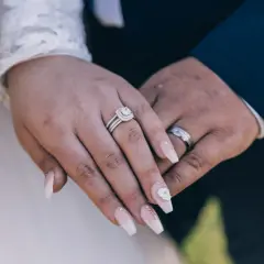 Dłonie nowożeńców z obrączkami i pięknymi paznokciami ślubnymi. Delikatny manicure zdobią kryształki i kwiat.