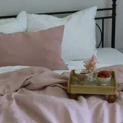 Ein rosafarbenes Leinenbett mit Kissen und einer Augenmaske. Ein Tablett mit Erdbeeren und Kaffee zeigt, wie wird leinen weich.
