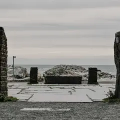 Kamienne filary i kamienna ława na placu przy morzu, jakby na **verdens ende**.