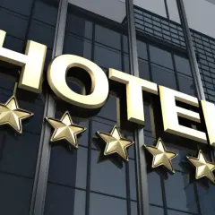 Złoty napis HOTEL i pięć gwiazdek na nowoczesnym, szklanym budynku. To zapowiedź luksusowego hotelu.