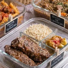 Carne asada con arroz, pasta con ternera y guiso de lentejas en recipientes de vidrio, listos para llevar.