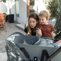Mama i synek pochylają się nad gondolą spacerówki, jakby zastanawiali się, od kiedy spacerówka będzie im potrzebna.