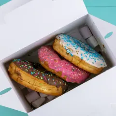 Pyszne opakowanie cukiernicze z trzema kolorowymi donutami: czekoladowym, różowym i białym z niebieską posypką.