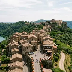 Borgo medievale sui Colli Albani, con case in pietra, un lago azzurro e uliveti rigogliosi.