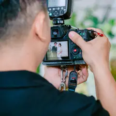 Fotograf trzyma aparat, na którego ekranie widać parę młodą.