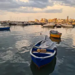 Barche nel porto al tramonto, con la città sullo sfondo. Un'atmosfera di pace e contemplazione, quasi un soffio di **santo spirito** sul mare calmo.