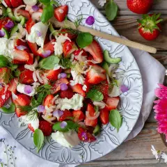 En härlig somrig sallad med jordgubbar, mozzarella, gurka och färska örter, dekorerad med ätbara blommor.