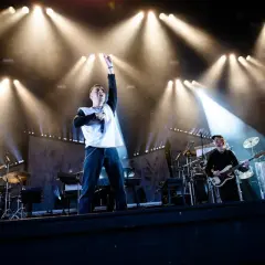 Oskar Linnros konsert med bandet upplyst av starka strålkastare. Sångaren med mikrofonen i handen och en arm uppsträckt.