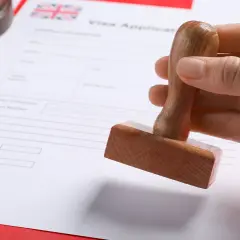 Dłoń trzyma pieczątkę nad formularzem wniosku o wizę do Anglii.